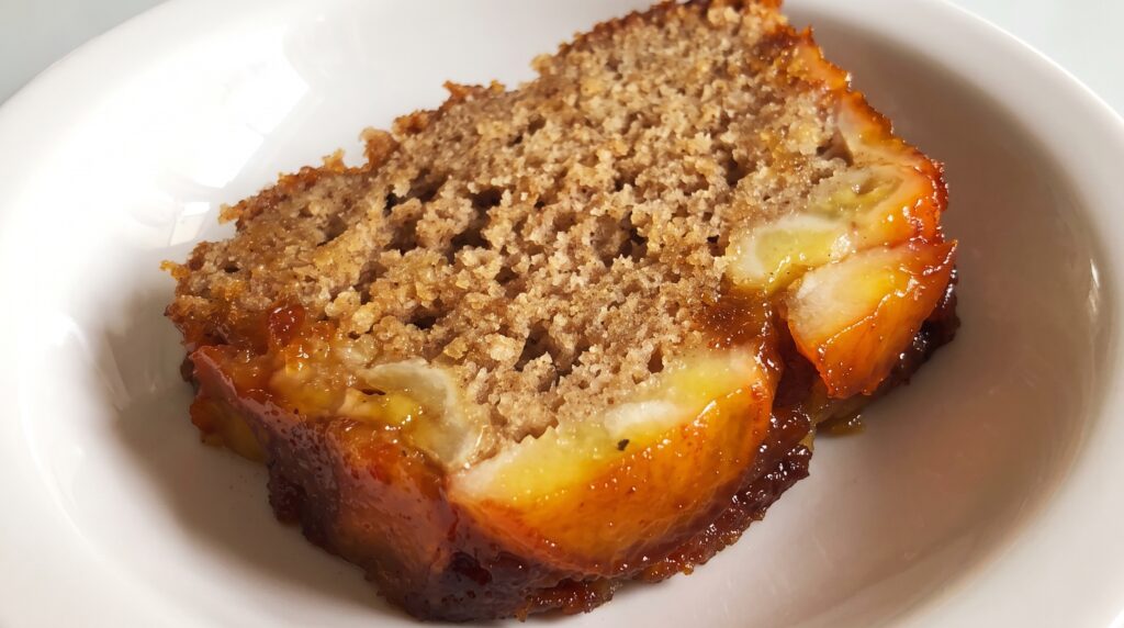 Fatia de bolo de banana caramelado mostrando a banana caramelizada por baixo e a massa úmida por dentro