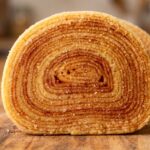Bolo de rolo cortado ao meio mostrando as camadas finissimas em espiral sobre tabua de madeira