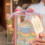 Confeiteira segurando caixa de bolo decorado embalada para entrega, com fita e etiqueta personalizada